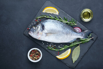 Raw dorado fish with spices on cutting board over black stone background. Copy space, top view.