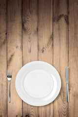 Empty white plate with knife and fork on a wooden table