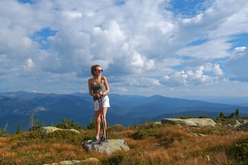 Young woman hiking up rock with sticks against a blue sky with clouds. A woman climbing on top of mountains.