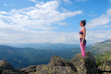 Naklejka premium Young woman hiking up hill against a blue sky with clouds. A woman jumps, dances, and climbs on top of mountains.