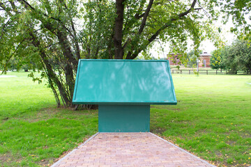 A green information stand with place for text stands in a summer park on a green lawn