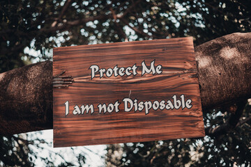 Front shot of an old tree with a board written protect me I am not disposable on it symbolic save tree and save nature photo