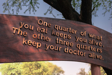 one quarter of what you eat keeps you alive. The other three quarters keep your doctor alive food and health quote on a wooden board in park