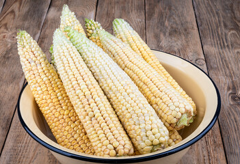 Peeled ears of corn in an enamel bowl.