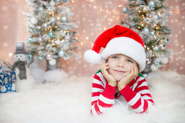 toddler boy in a Christmas hat laying down on the floor next to the Christmas tree 