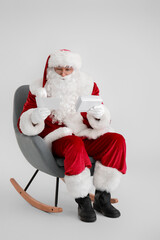 Santa Claus with letters sitting in armchair on light background