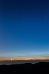 Moon and Neowise comet at dusk on a blue sky above mountains