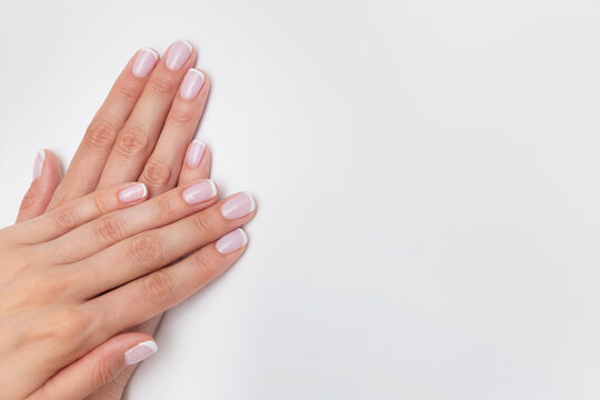 French manicure. Nude nails covered with gel polish on a white background with copy space. Natural manicure with camouflage base. Female hands close up, beauty salon concept