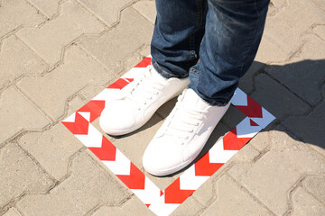 Man standing on taped floor marking for social distance outdoors, closeup. Coronavirus pandemic