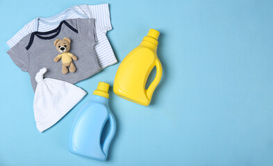 Flat lay composition with bottles of detergent and children's clothes on light blue background. Space for text