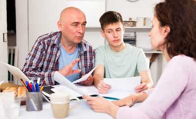Young man with his wife and teen son reading documents at home table