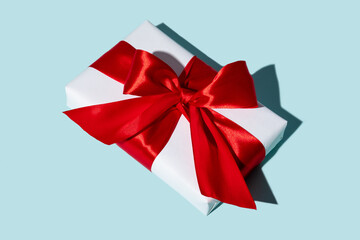 Holiday gift. Special occasion reward. Care package. Festive surprise. Present wrapped in white box with red ribbon bow isolated on blue background.