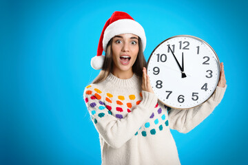 Woman in Santa hat with clock on light blue background. Christmas countdown