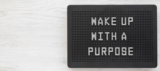 'Wake up with a purpose' words on a black lightbox on a white wooden background, top view. From...