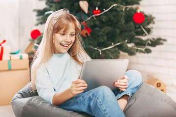 A beautiful little blonde with a European appearance communicates via a mobile tablet by video call with friends and grandparents at Christmas.