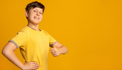 Like gesture. Satisfied child. Well done. Victory success. Portrait of enthusiastic happy young fan boy in yellow t-shirt supporting with thumb up isolated on orange copy space advertising background.