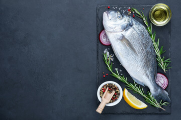 Raw dorado fish with olive oil, rosemary and spices on cutting board over black stone background....
