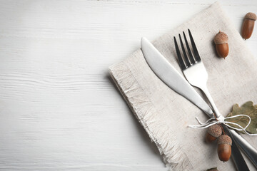 Cutlery, acorns and napkin on white wooden background, flat lay with space for text. Table setting elements