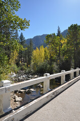 Fototapeta premium Vertical shots of a bridge over a river, and mountains framed by fall colors in the background