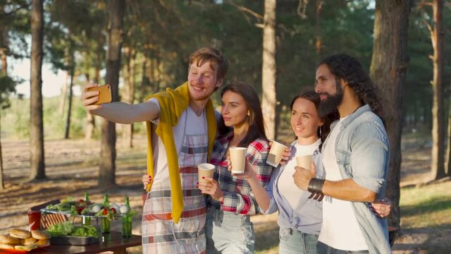 Young women and men taking a selfie with the phone. People enjoying a picnic in nature.