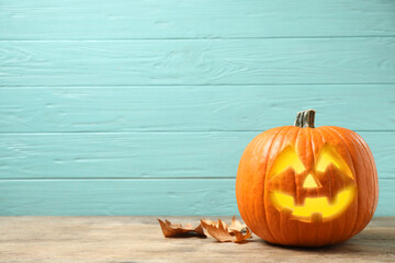 Scary jack o'lantern pumpkin on light blue wooden background, space for text. Halloween decor