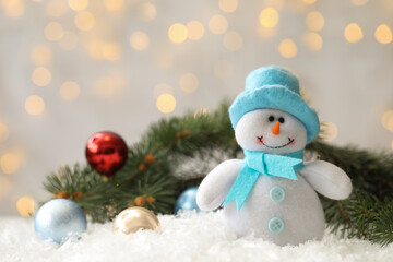 Snowman toy and Christmas balls on snow against blurred festive lights. Space for text