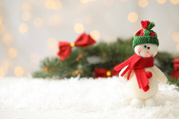 Snowman toy on snow against blurred festive lights, space for text. Christmas decoration