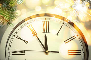Obraz na płótnie Canvas Clock showing five minutes till midnight with fir tree branches and sparkler, closeup with bokeh effect. New Year countdown