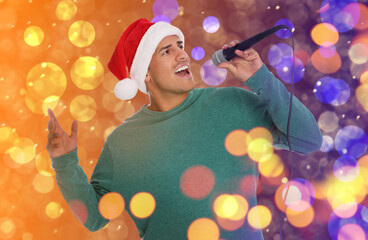 Happy man in Santa hat singing on bright background, bokeh effect