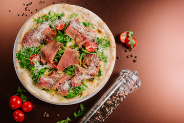 Fresh baked pizza with ham and green herbs on wooden background