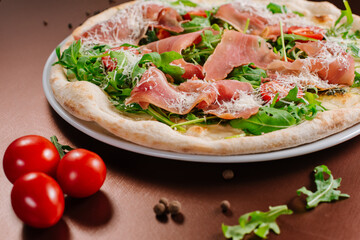 Fresh baked pizza with ham and green herbs on wooden background