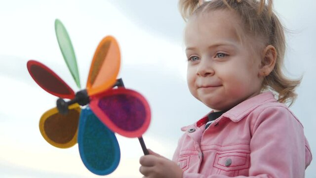 little daughter girl play pinwheel a wind toy. happy family concept. child plays with windmill. portrait girl kid blonde holds flower toy spinning pinwheel. lifestyle happy childhood