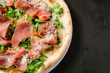Fresh baked pizza with ham and green herbs on wooden background