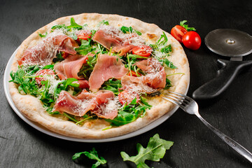 Fresh baked pizza with ham and green herbs on wooden background