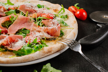 Fresh baked pizza with ham and green herbs on wooden background