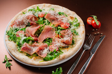 Fresh baked pizza with ham and green herbs on wooden background