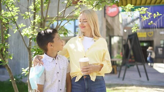 Portrait of cheerful woman with son in street, young blonde woman went for walk on sunny day, breathe fresh air after quarantine.