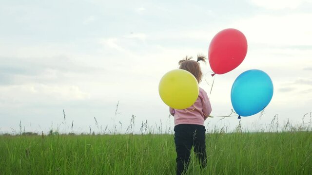 daughter little girl fun runs with balloons a on her birthday outdoors by field. dream happy family concept. child girl kid day. child is running and balloons on a background of blue sky caring for a
