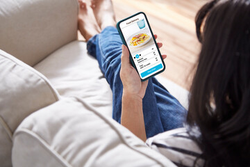 women holding phone with application delivery food online sit on couch at home