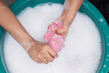 Fototapeta premium Female hands wash clothing by hand with detergent in basin. selective focus and space for text.