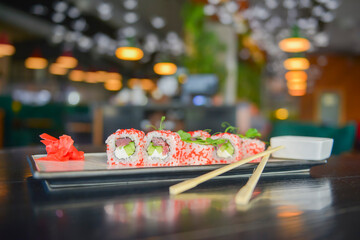 Salmon and caviar sushi rolls served on a traditional plate on a wooden table in a restaurant.