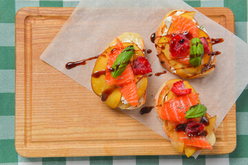 Delicious fruit salmon bruschetta with sauce served on a wooden board over green plaid table cloth.