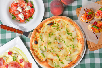 Restaurant or bar table with traditional Italian food. Pizza, salad and brischetta over green plaid table cloth.