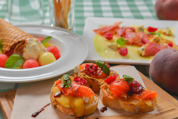 Delicious fruit salmon bruschetta with sauce served on a wooden board over green plaid table cloth.