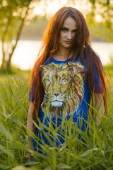 Wild girl in the grass, looks straight. She is wearing a blue T-shirt with a painted lion.