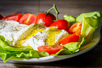 Italian buffalo mozzarella cheese with cherry tomatoes and extra virgin olive oil served on green lettuce leaves