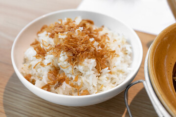 Steamed rice topped with fried shallots, serving on white bowl.