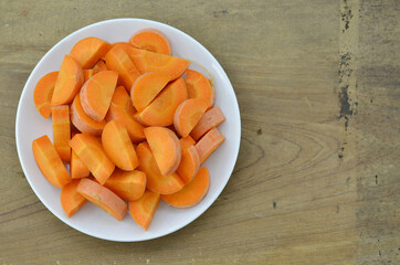 Cut carrots thick in white plate on wooden background