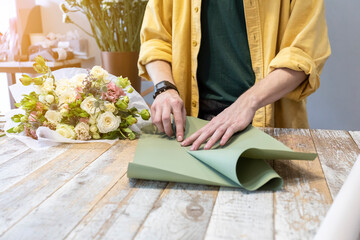 A male florist decorates a flower bouquet in a flower salon.