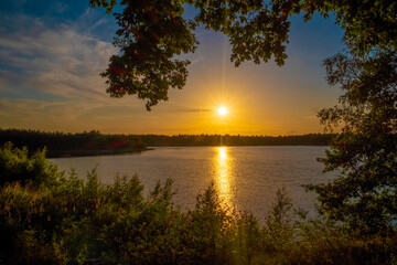 Fototapeta na wymiar Panorama of a gorgeous sunset at a forest lake, with gold and blue color in the sky and trees reflected in the water. High quality photo